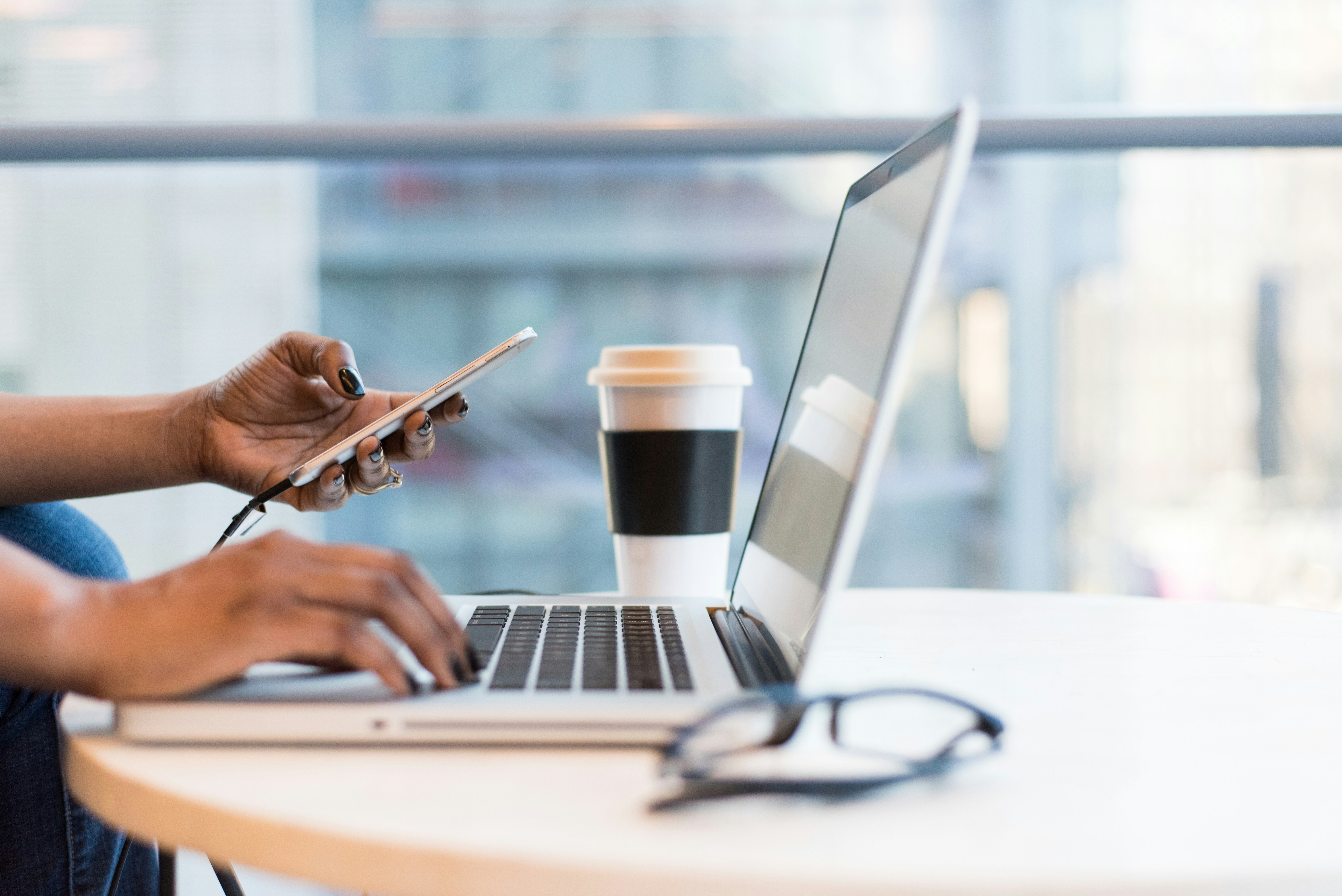 Person working on a laptop with a phone and coffee